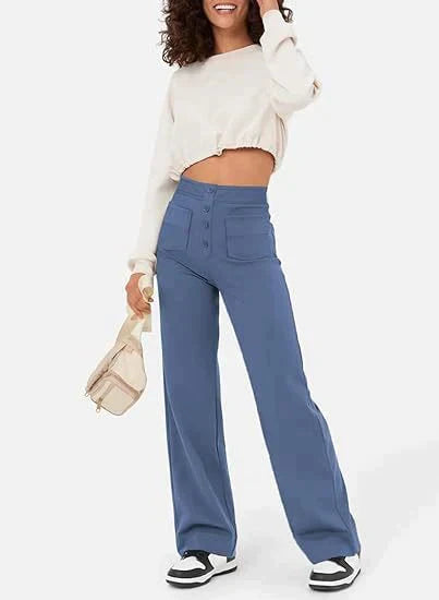 Frau in blauer, hoch taillierter, elastischer Hose und weißem Pullover, hält beige Tasche.