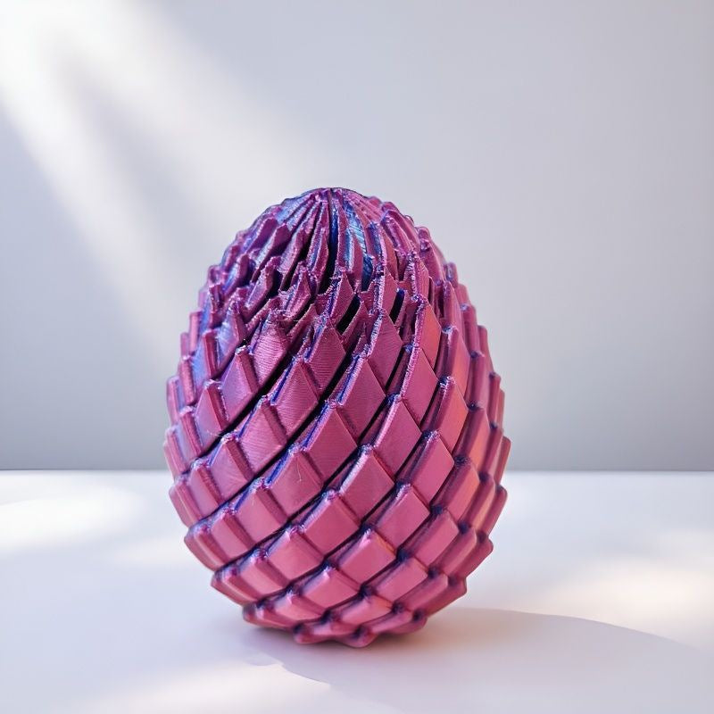 Drachenei in glänzendem Violett-Pink auf weißer Fläche, seitlich von Sonnenlicht und Schatten gestreift. 10