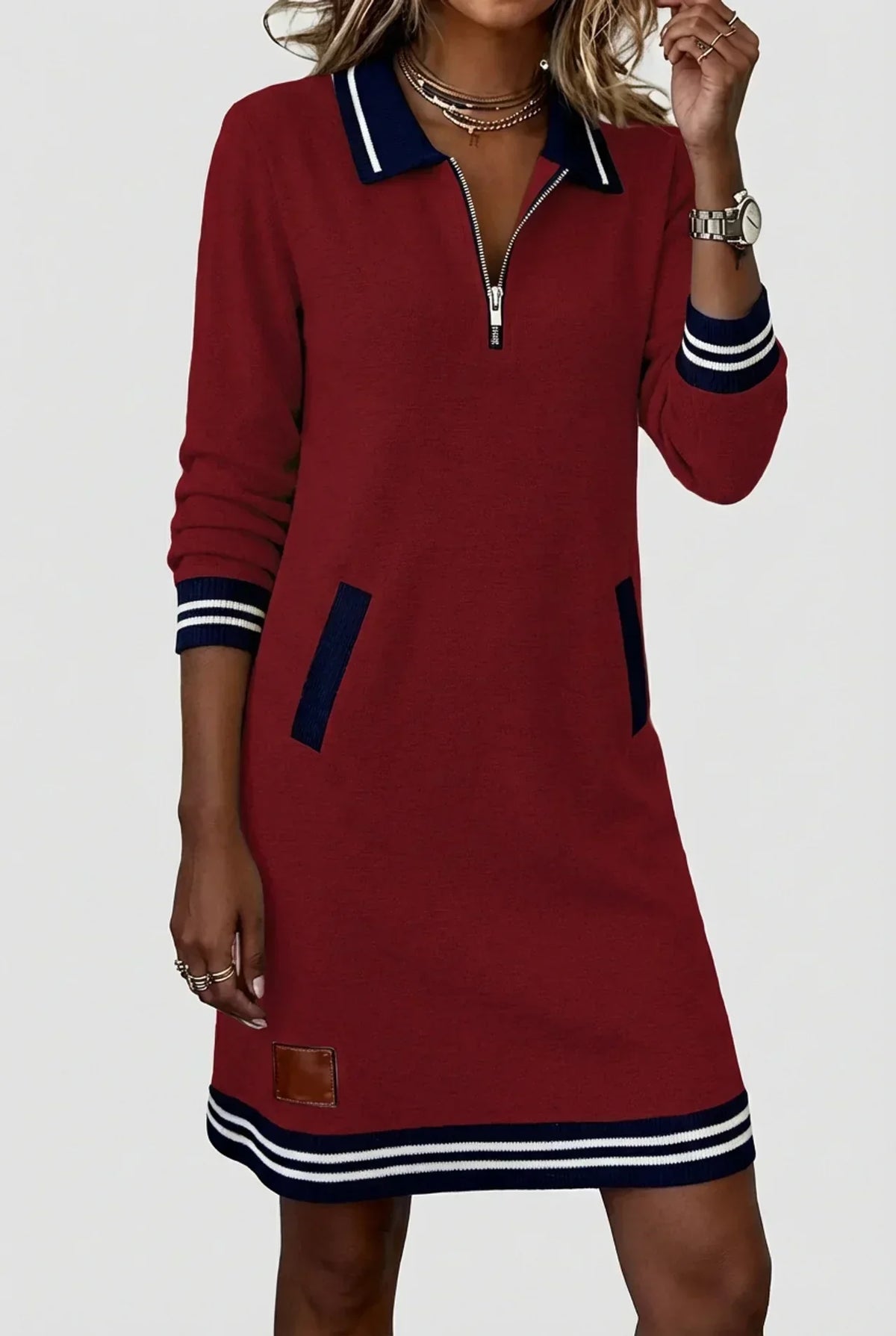Weinrotes Kleid mit Streifenkragen, Reißverschluss und marineblauen Taschenbesätzen, Streifensaum und Lederpatch unten sichtbar.