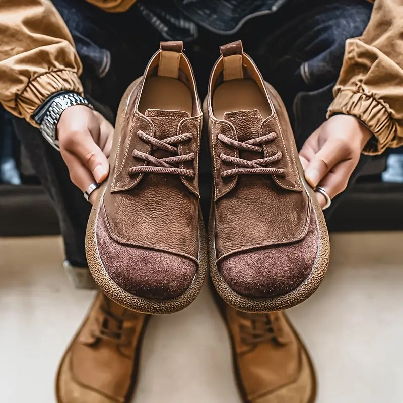 Dunkelbraune orthopädische Komfortschuhe, ein Paar von vorn in den Händen gehalten.