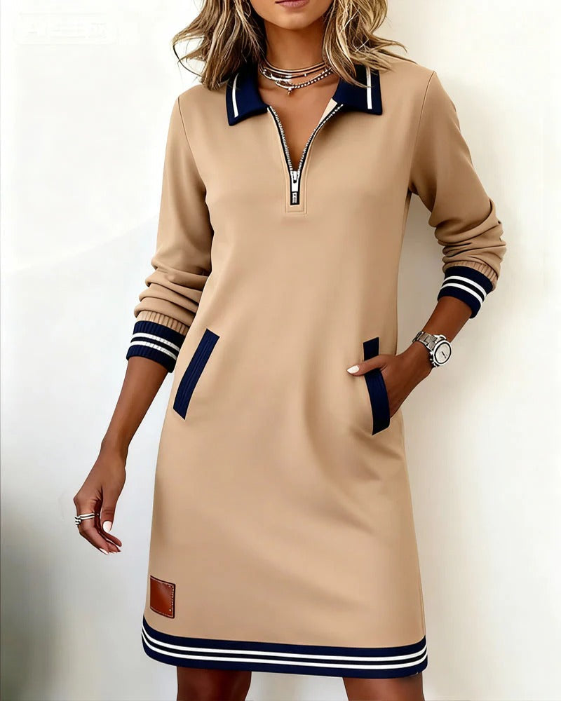 Beigefarbenes Kleid mit dunkelblauem Reverskragen und Reißverschluss, vom Model getragen, eine Hand in der Tasche, Lederpatch am Saum. 3
