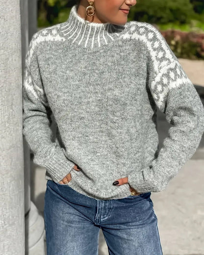 Grauer Strickpullover mit Stehkragen und weißem Zierstreifen über den Schultern, getragen zur Jeans vor einer Säule. 5