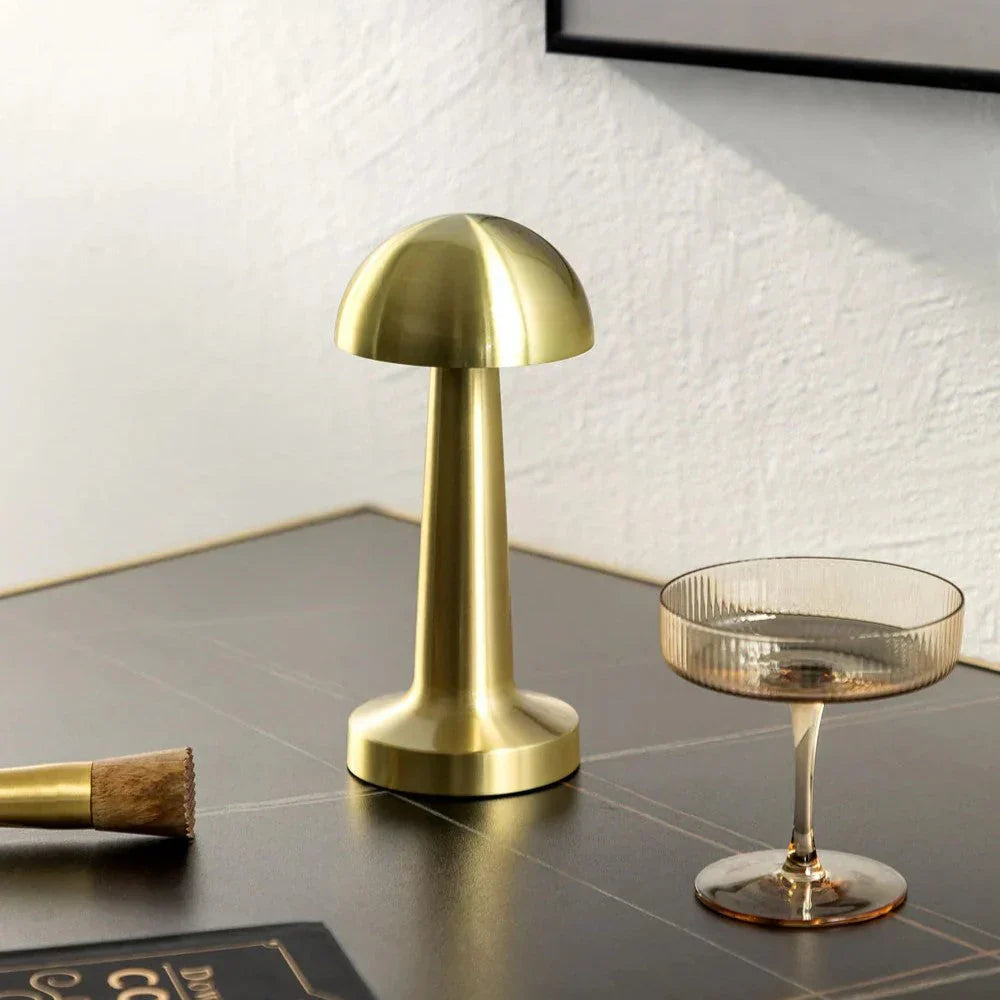 Goldene kabellose LED-Tischlampe, Pilzform, modern, auf Holzoberfläche, neben Glas.