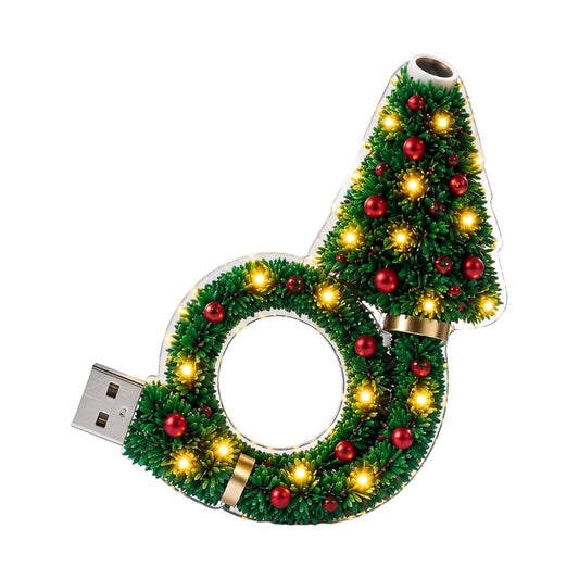 Freigestellte Frontansicht der Projektorlampe: Tannenzweig-Kranz mit roten Kugeln, warm leuchtenden Lichtern, USB-Stecker links und Linse an der Baumspitze. 1