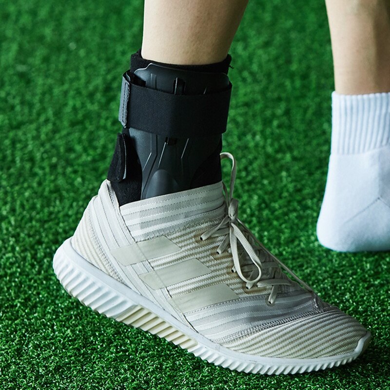 Person mit Knöchelbandage und Sportschuh auf grünem Kunstrasen.