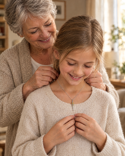 Großmutter legt einem lächelnden Mädchen im cremefarbenen Pullover die Kette mit dem silber-goldenen Anhänger um den Hals. 4