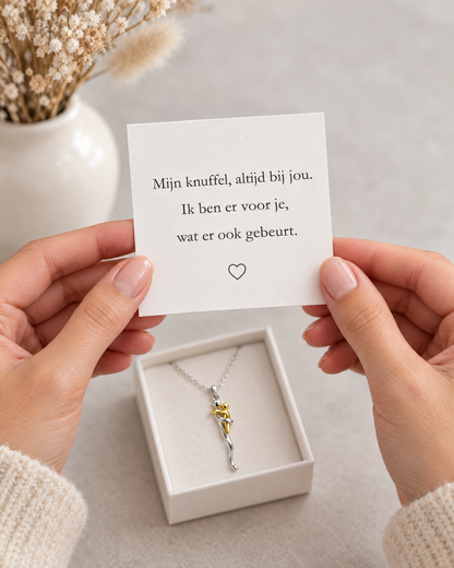 Hände halten eine Grußkarte mit Herz über einer geöffneten Geschenkbox, in der die Halskette mit Anhänger liegt. 6