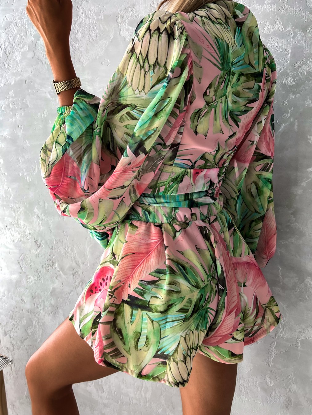 Frau in grün-rosa tropischem Kleid mit Blattmuster, Sommermode, elegantes Design.