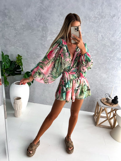 Frau im grünen-rosa Sommerkleid mit tropischem Muster, steht in modernem Wohnzimmer.