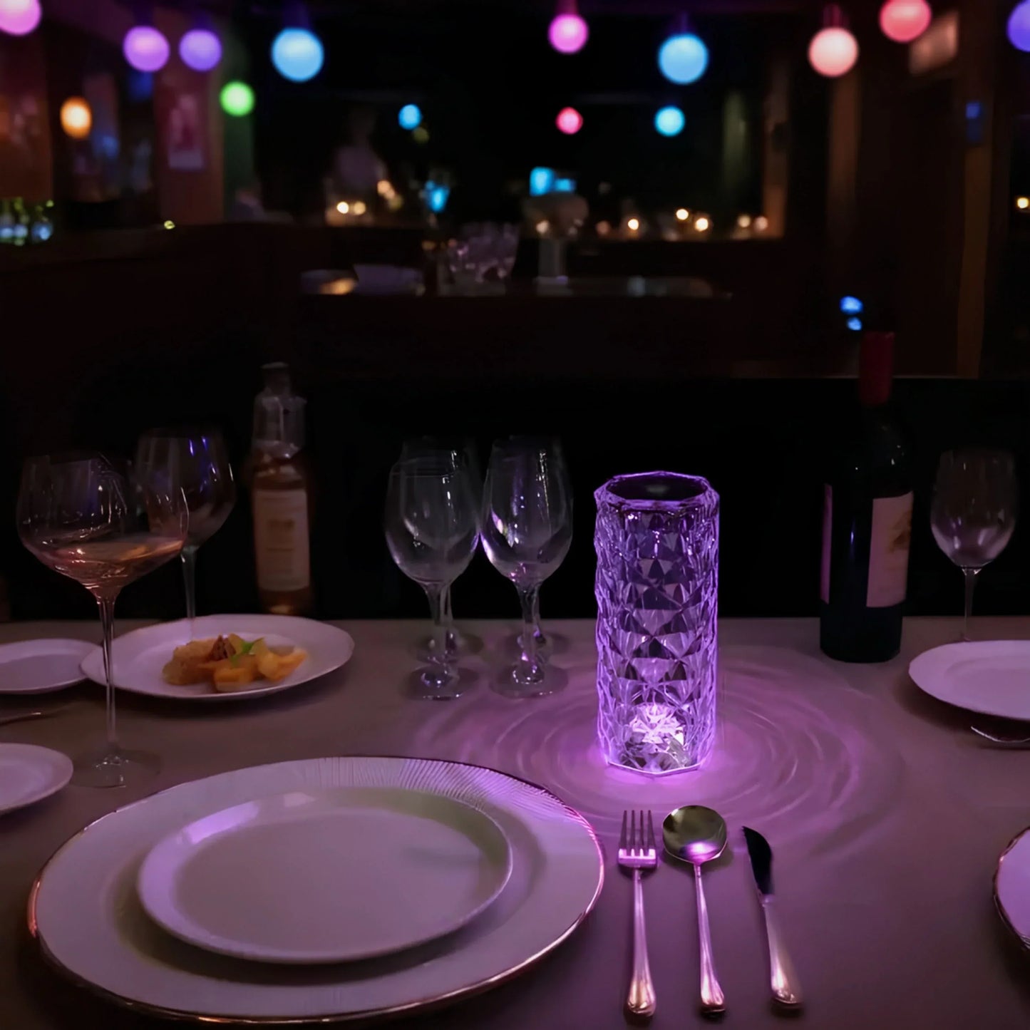 Elegantes Abendessen mit Kristallvase, Weingläsern und bunter Beleuchtung im Hintergrund.