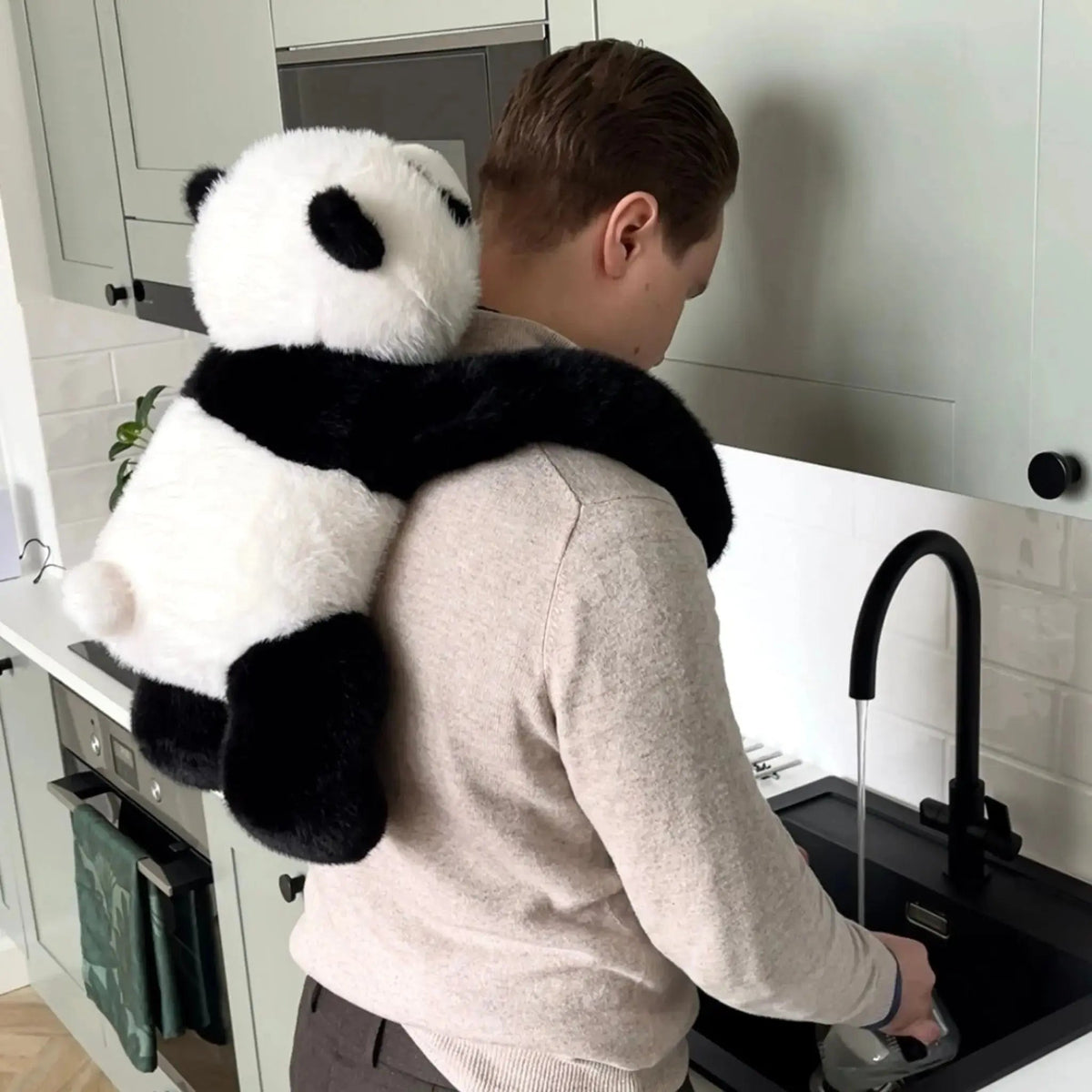 Detail des Panda-Plüschtiers mit langen Armen auf den Schultern eines Mannes in der Küche