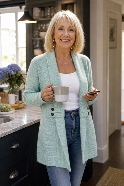 Lächelnde Frau in der Küche trägt die mintgrüne Strickjacke mit Tasse und Smartphone in der Hand 4