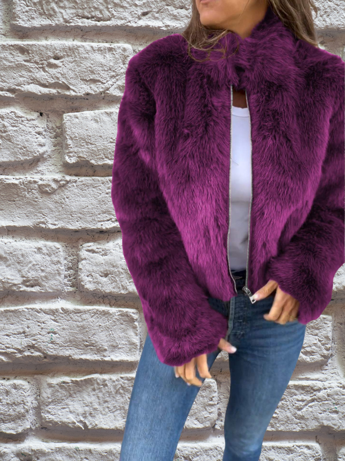 Frau in lila Kunstpelzjacke vor Ziegelwand, modisch, warm, Winterkleidung.