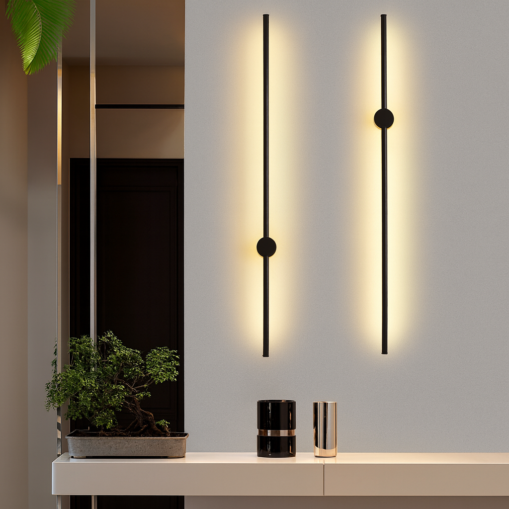 Zwei schwarze Stab-Wandleuchten mit warmem Lichtschein an grauer Wand über einem hellen Sideboard mit Bonsai und Vasen.