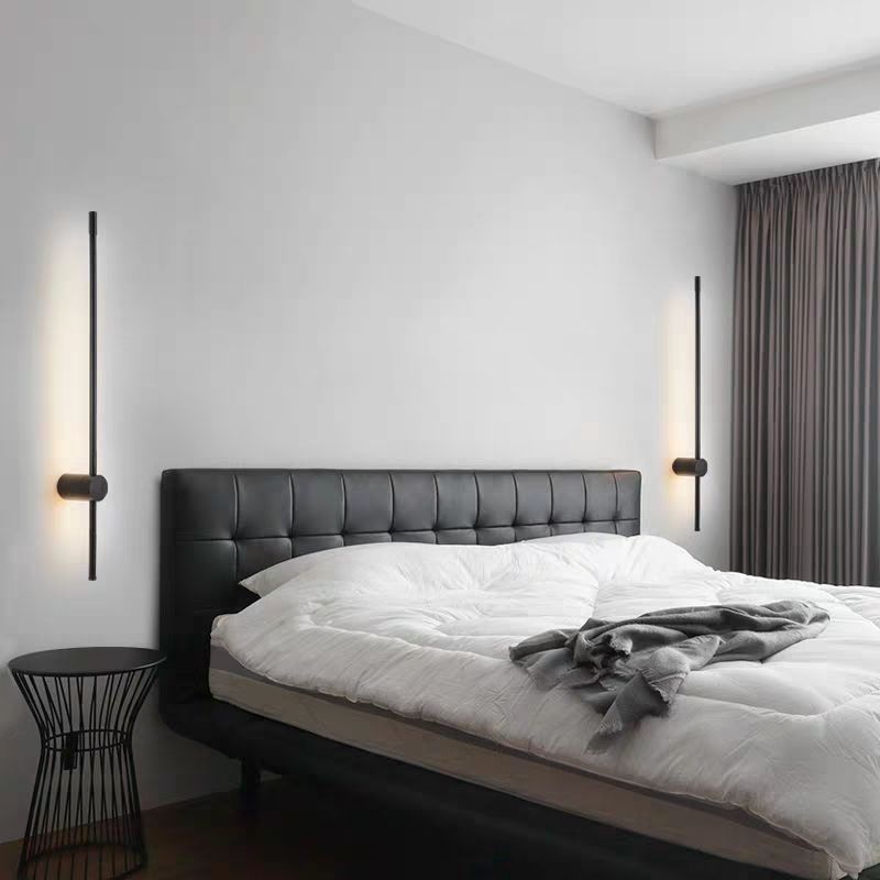 Zwei schwarze Stab-Wandleuchten als Bettlicht links und rechts über einem Bett mit gestepptem schwarzem Kopfteil im Schlafzimmer.