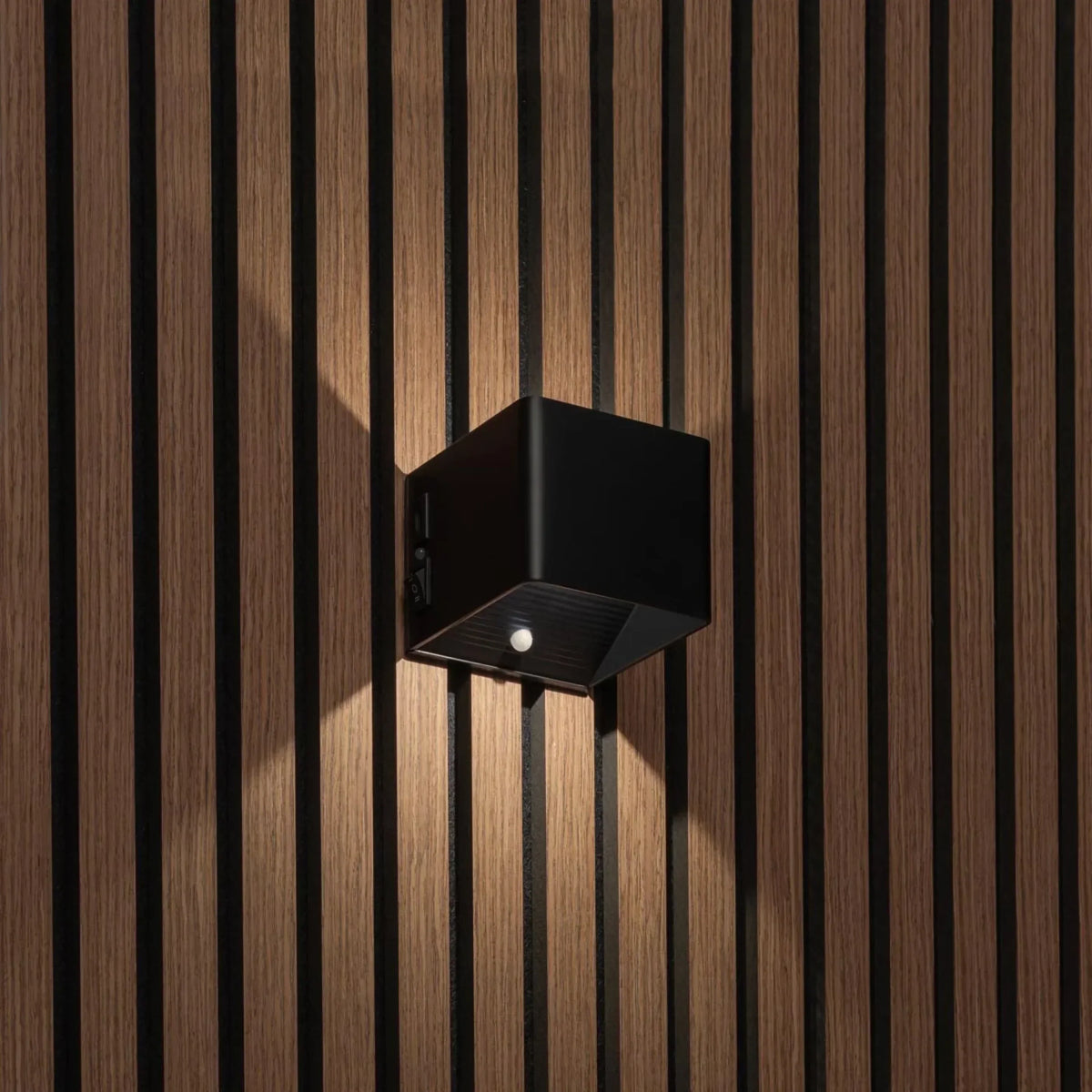 Schwarze würfelförmige Wandleuchte an Holzlamellenwand, Seitenansicht mit Schalter und Bewegungssensor an der Unterseite 1
