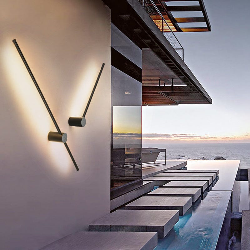 Zwei schräg gedrehte schwarze Stableuchten an einer hellen Wand mit Blick auf Meer und Infinity-Pool in der Abenddämmerung. 2