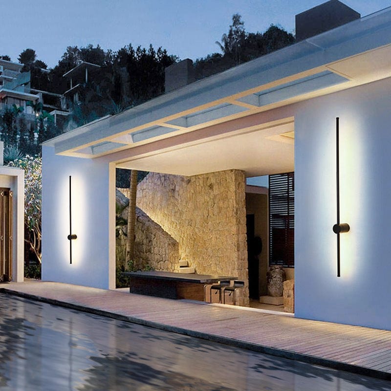 Zwei senkrechte schwarze LED-Leuchten beidseits eines offenen Terrassenbereichs mit Natursteinwand, davor ein Pool, im warmen Abendlicht. 3