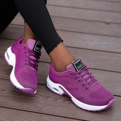 Violette Sneaker mit Schnürung und weißer Dämpfungssohle, getragen zu schwarzer Leggings.