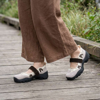 Beige Slipper mit braunem Klettriemen auf einem Holzsteg, getragen zu weiter brauner Leinenhose.