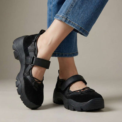 Schwarze Slipper aus Veloursleder mit Klettriemen und kräftiger Profilsohle, im Studio zu Jeans getragen.