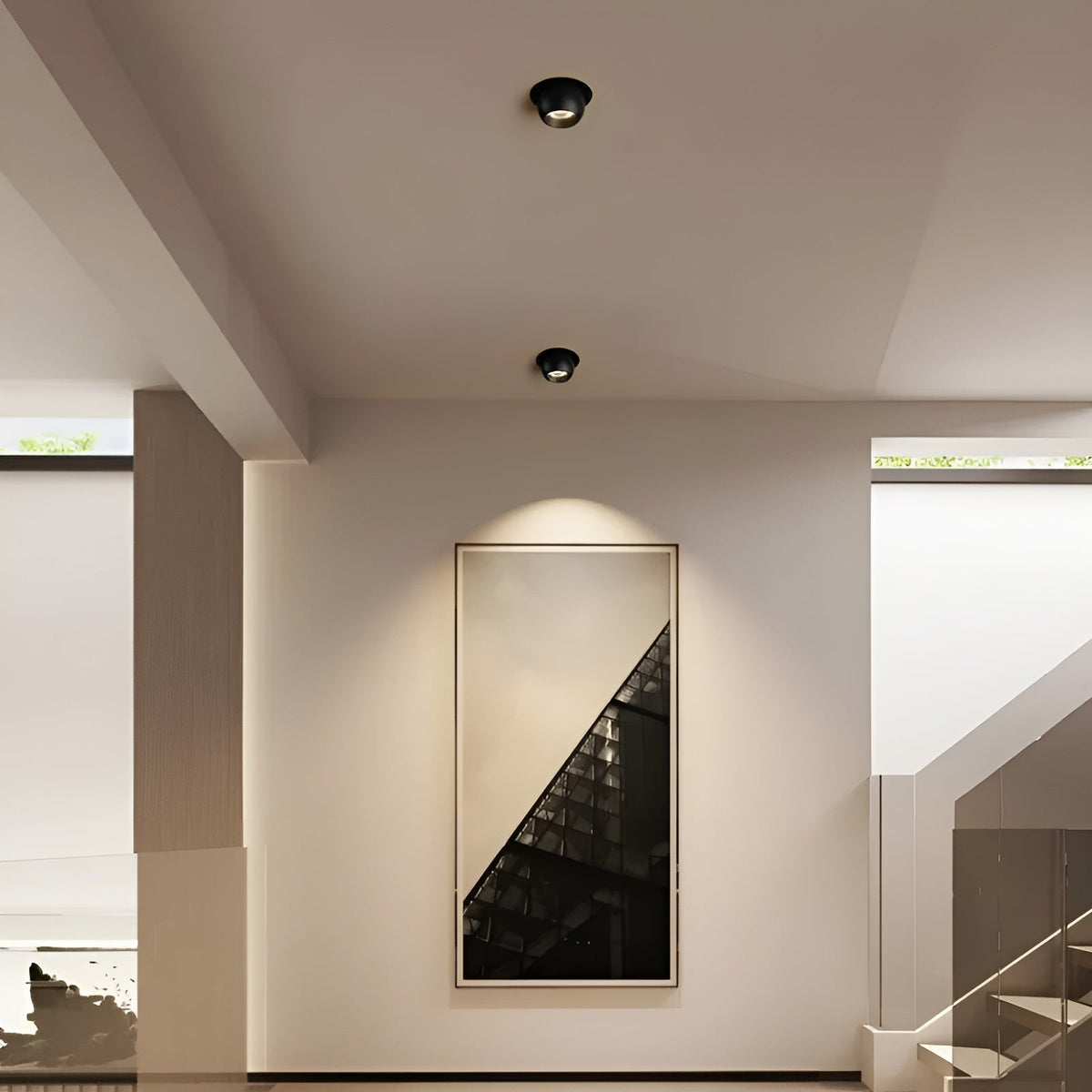 Zwei schwarze Einbaustrahler an der Flurdecke setzen ein gerahmtes Wandbild neben der Treppe in Szene 3