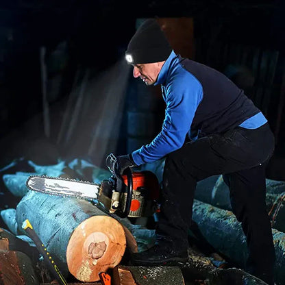 Mann mit Stirnlampe sägt Holzstamm mit Kettensäge in dunkler Umgebung.