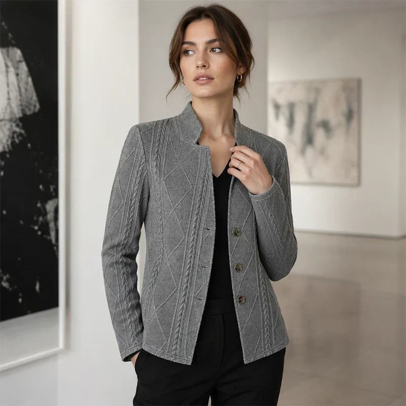 Frau im grauen Blazer mit Zopfmuster über schwarzem V-Ausschnitt-Oberteil, Hand in der Hosentasche, in einer Galerie. 11