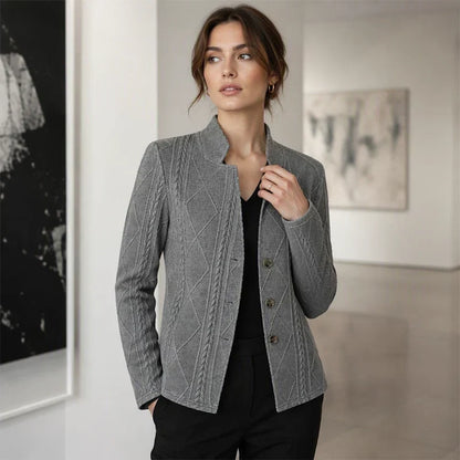 Frau im grauen Blazer mit Zopfmuster über schwarzem V-Ausschnitt-Oberteil, Hand in der Hosentasche, in einer Galerie. 11