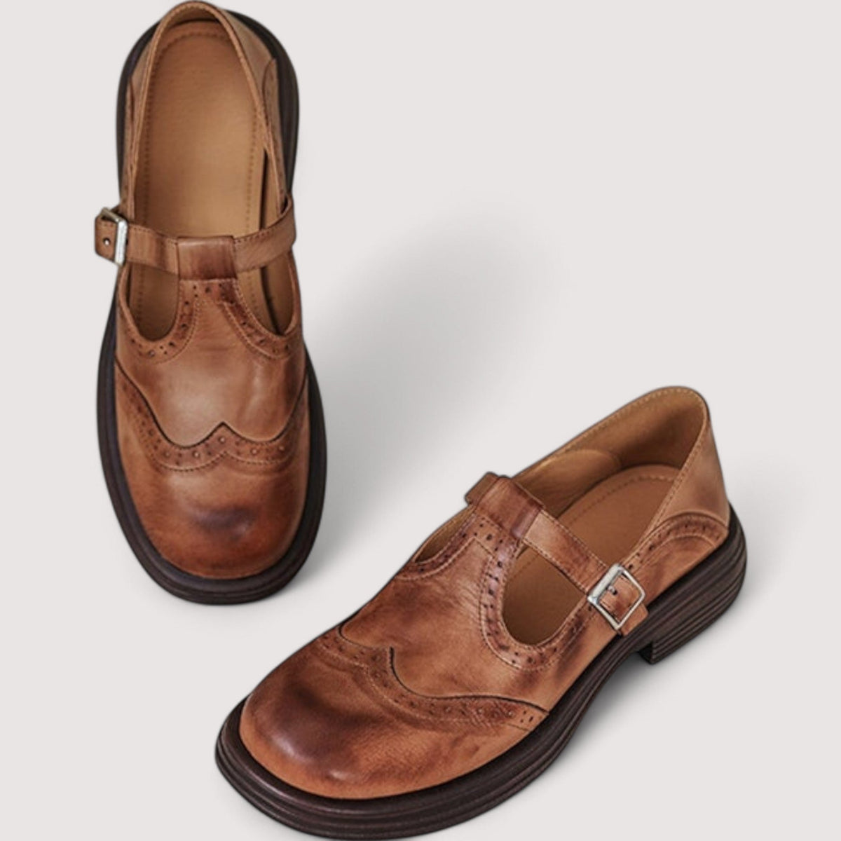Braune Leder-Mary-Jane-Ballerinas mit Lochmuster, Schnallenriemen und profilierter Sohle, schräg von oben.