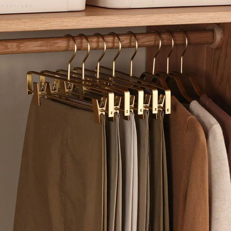 Mehrere goldfarbene Hosenbügel mit eingeklemmten Hosen hängen im Kleiderschrank an einer Holzstange 3