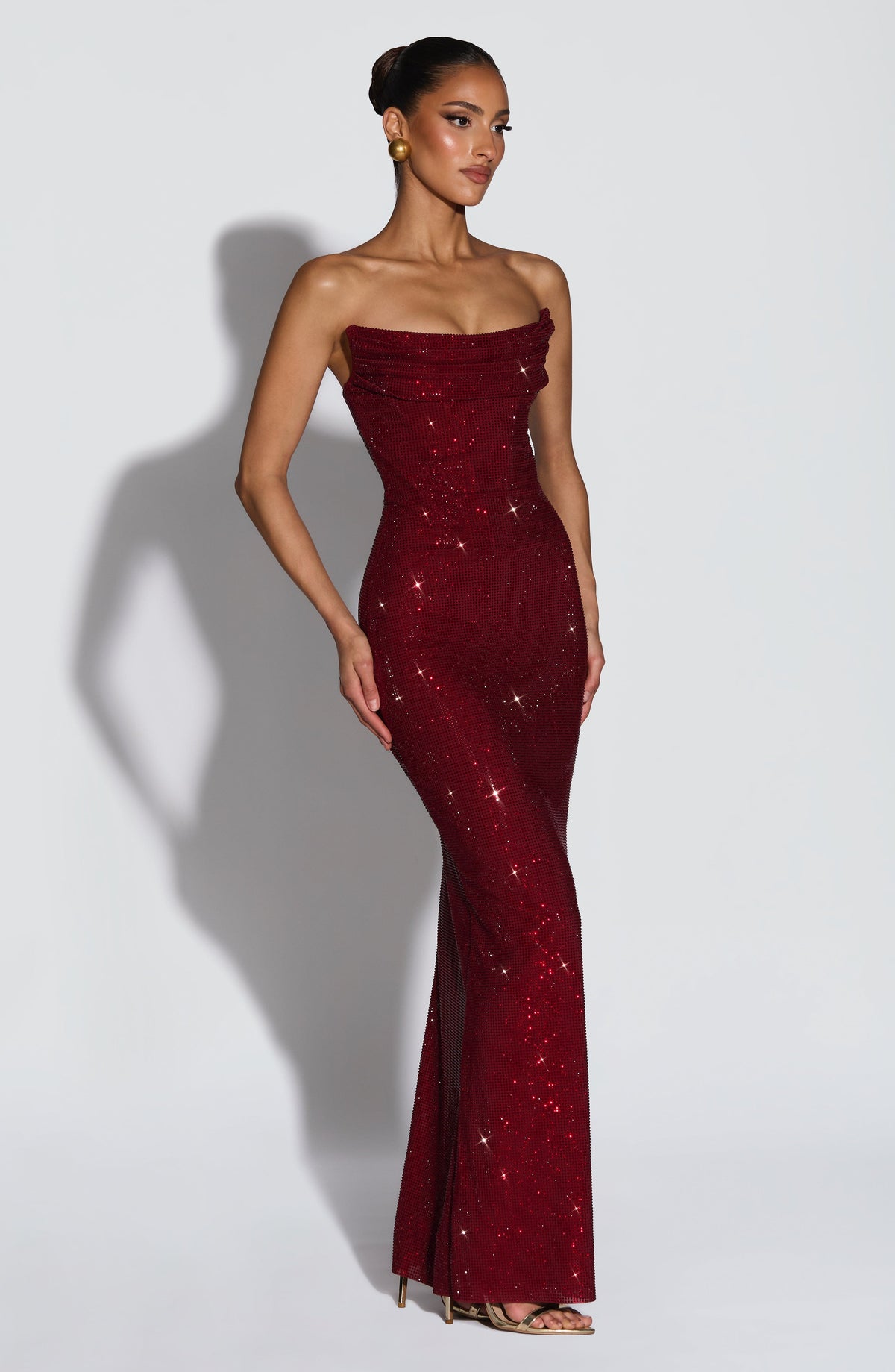 Dunkelrotes Kleid schräg von vorne, figurbetonter langer Schnitt mit Strassbesatz und goldenen Sandaletten. 4