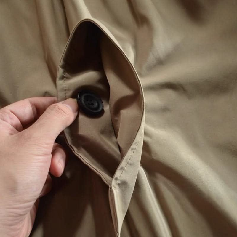 Detailaufnahme einer Manteltasche in Beige, eine Hand zieht die Tasche auf und zeigt den schwarzen Knopf im Inneren. 8