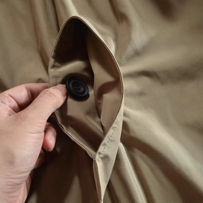 Detailaufnahme einer Manteltasche in Beige, eine Hand zieht die Tasche auf und zeigt den schwarzen Knopf im Inneren. 8