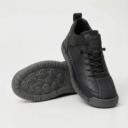 Schwarzer Sneaker mit genarbter Oberfläche und Schnürung, ein zweiter Schuh liegt mit der grauen Profilsohle nach oben. 3