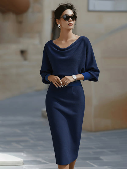 Frontansicht: Model mit Sonnenbrille in marineblauem Strickkleid mit Wasserfallausschnitt, Fledermausärmeln, kontrastierenden Bündchen und engem Rock. 6