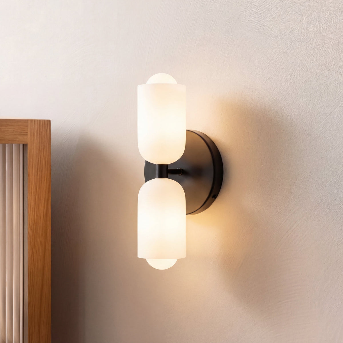 Schwarze Wandleuchte mit zwei milchigen Glaszylindern in Seitenansicht, daneben ein Holzrahmen mit Riffelglas.