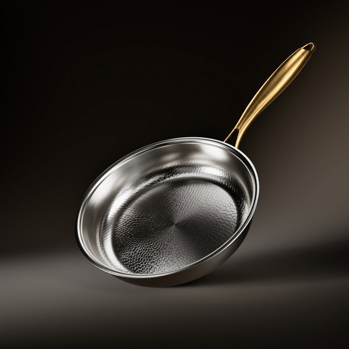 Von Hand gehämmerte Titan-Bratpfanne in Silber mit goldfarbenem Griff, schräg vor dunklem Hintergrund.