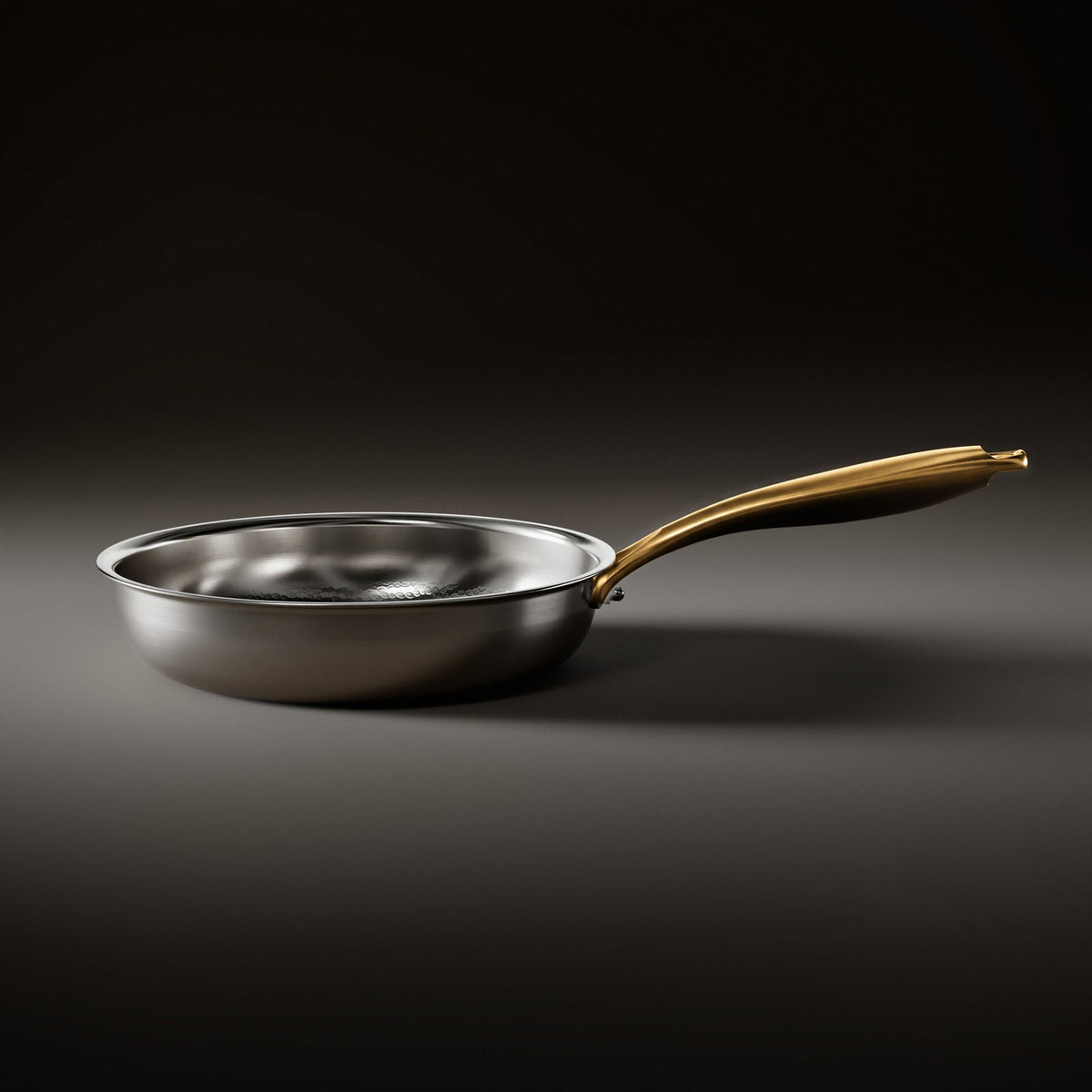 Seitenansicht der Titan-Bratpfanne in Silber mit goldfarbenem Griff auf dunklem Untergrund.