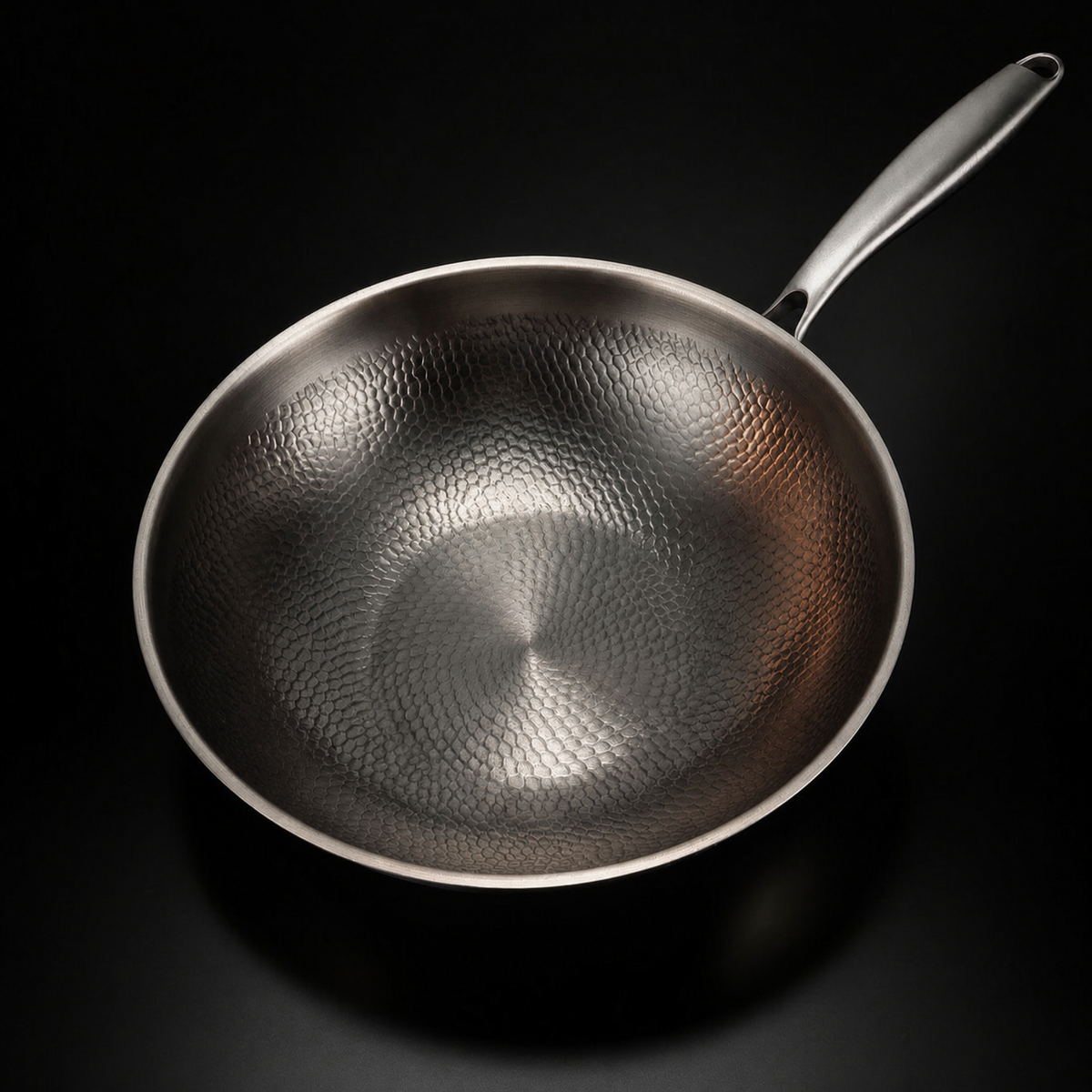 Draufsicht in die leere Wokpfanne aus Titan mit gleichmäßigem Hammerschlagmuster und langem Metallgriff.