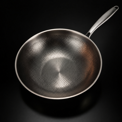Draufsicht in die leere Wokpfanne aus Titan mit gleichmäßigem Hammerschlagmuster und langem Metallgriff.