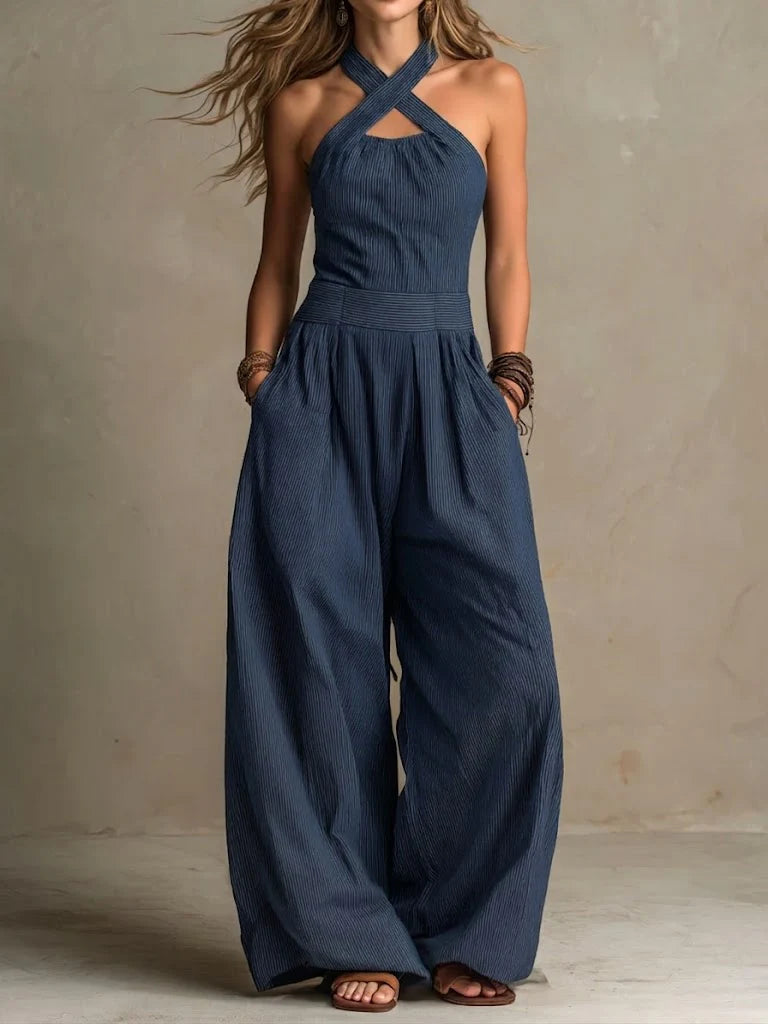 Frau trägt den Jumpsuit in Marineblau mit feinen Streifen, überkreuztem Neckholder-Ausschnitt, breitem Bund und weiten Hosenbeinen. 3