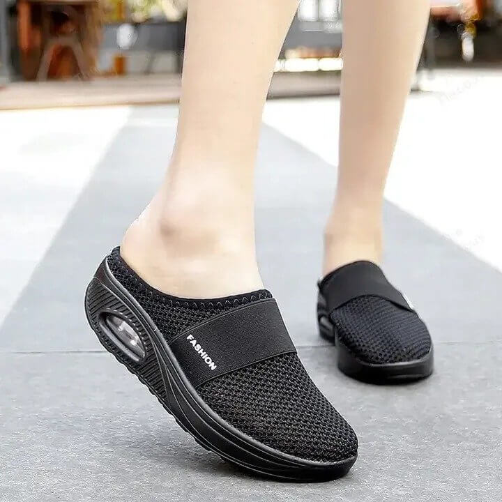 Schwarze Netz-Slipper mit Luftkissen-Sohle, im Gehen an den Füßen einer Frau auf der Straße 3