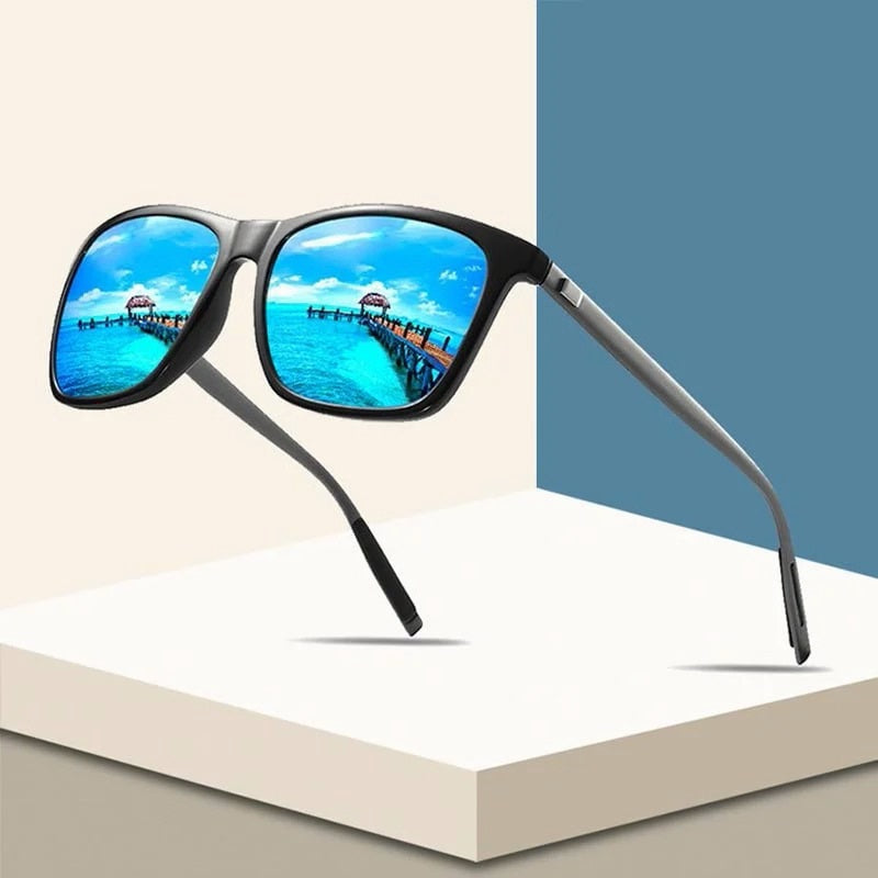 Schwarze Sonnenbrille mit blau verspiegelten Gläsern schwebt vor beigem und blauem Hintergrund, Steg am Meer spiegelt sich 1