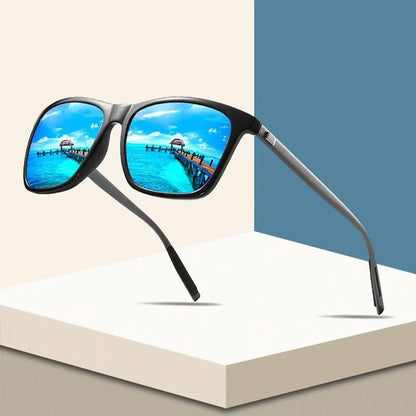 Schwarze Sonnenbrille mit blau verspiegelten Gläsern schwebt vor beigem und blauem Hintergrund, Steg am Meer spiegelt sich 1