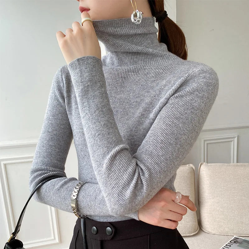 Hellgrauer Rollkragenpullover am Model, Seitenansicht mit Pferdeschwanz, kombiniert mit schwarzer Hose und Handtasche 7