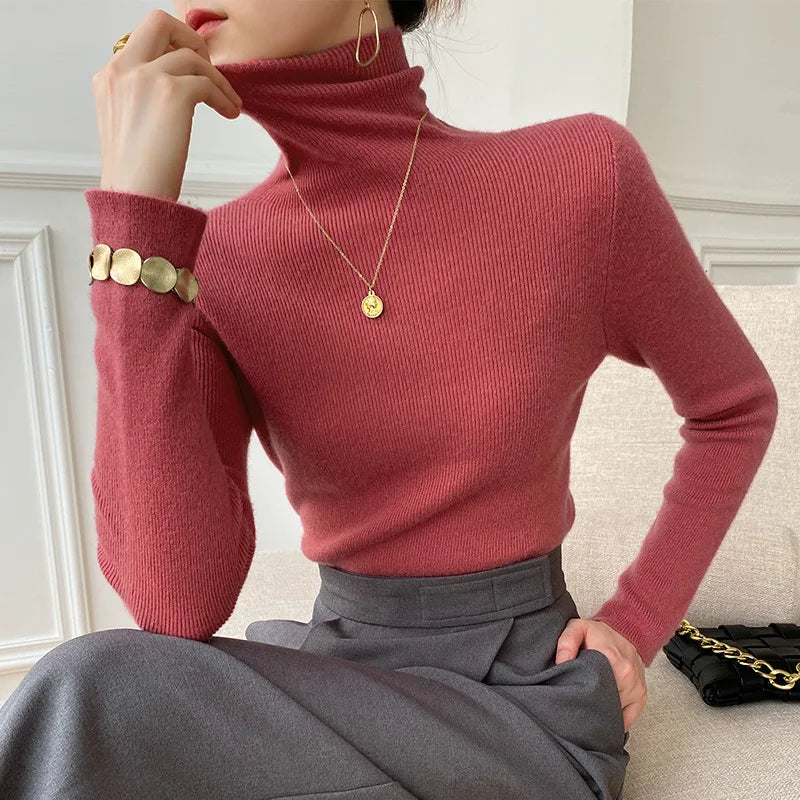 Rotbrauner Rollkragenpullover am Model, kombiniert mit grauem Rock, goldener Kette und Armschmuck, Hand am Kinn 2