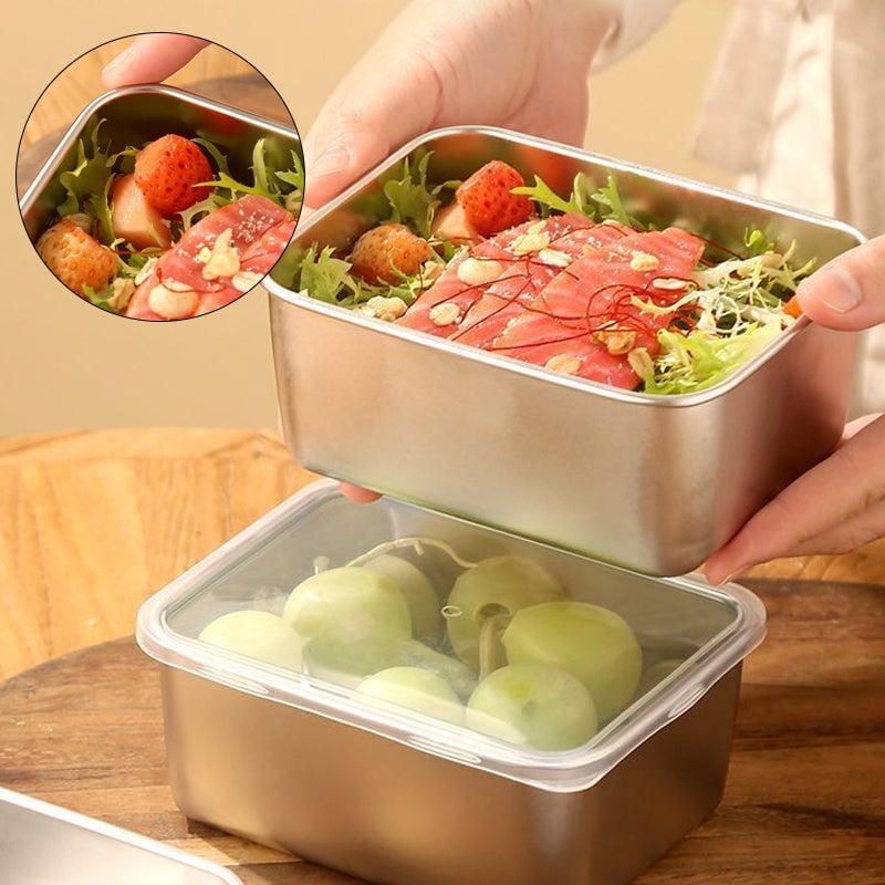 Hände halten eine Edelstahlschale mit Lachs, Salat und Erdbeeren über einer Box mit durchsichtigem Deckel und Trauben, Detailausschnitt oben links. 1