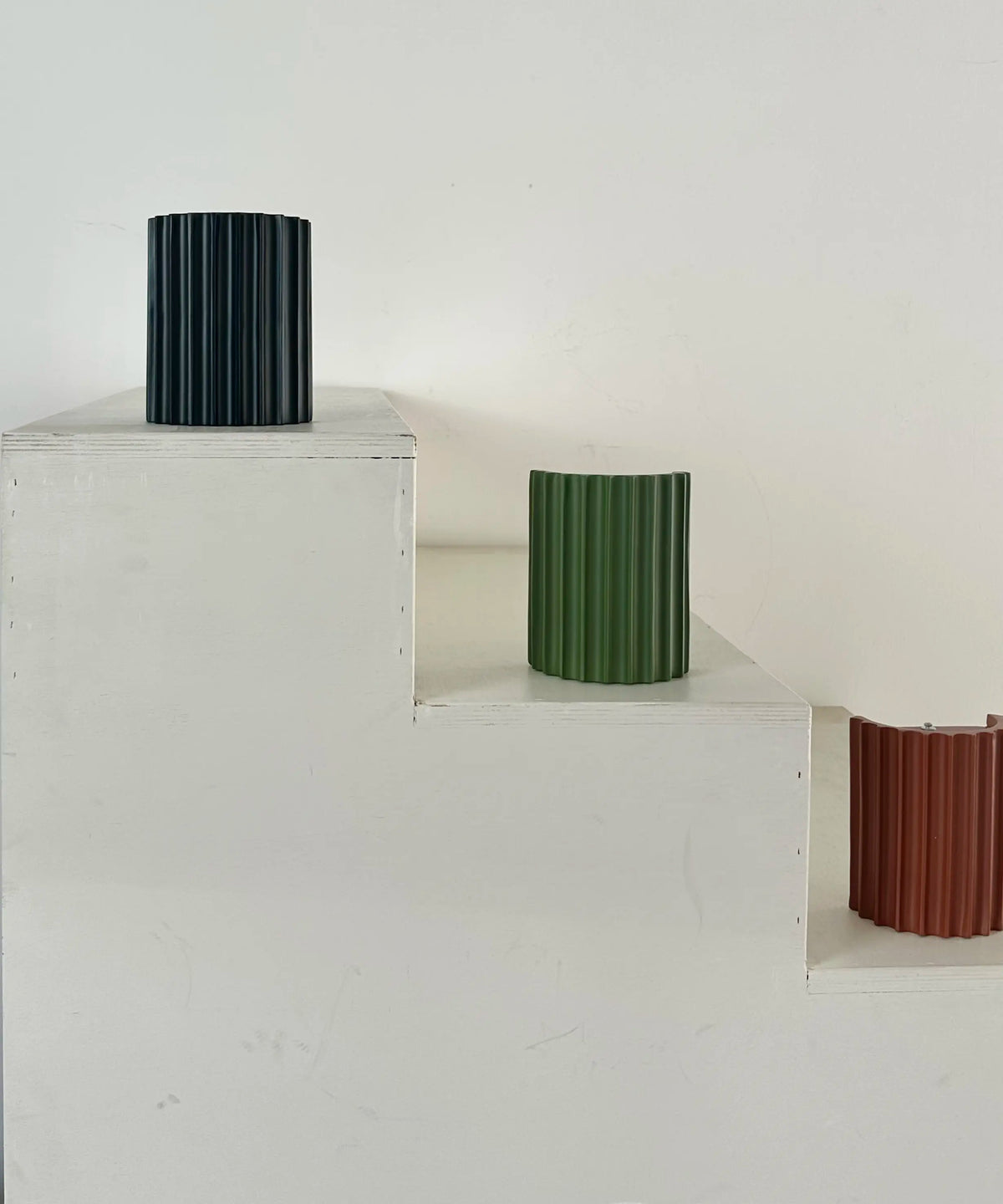 Lampengehäuse in Schwarz, Grün und Terrakotta auf weißen Stufen, das terrakottafarbene mit sichtbarer Rückseite 11