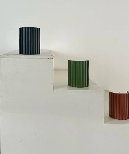 Lampengehäuse in Schwarz, Grün und Terrakotta auf weißen Stufen, das terrakottafarbene mit sichtbarer Rückseite 11